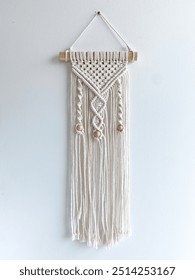 Wall Hanging Macrame made of white cotton rope filled with wooden beads hanged on the white wall 