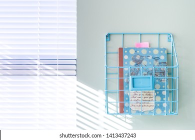 Wall Hanging Wire Basket Holding A Notebook In A Bright Home Office, Next To A Window, On A Mint Green Painted Wall.