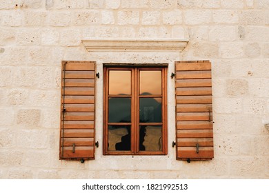 The Wall Of The House Is White Brick With New Brown Wooden Shutters And A Tinted Window.