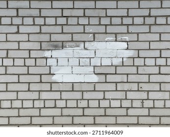 A wall made of gray bricks shows patches of white paint in an urban area under daylight.