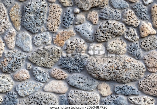 Wall is made of natural porous stone.\
Grey natural background. stone. Texture of natural porous . Topic -\
wall of house or fence in Mediterranean\
style