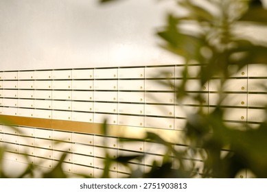 A wall of mailboxes featuring numerous compartments, partially obscured by green foliage in the foreground, creating a layered visual effect