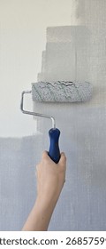 Wall painting with roller using gray paint on white surface. Fresh paint and DIY home renovation concept