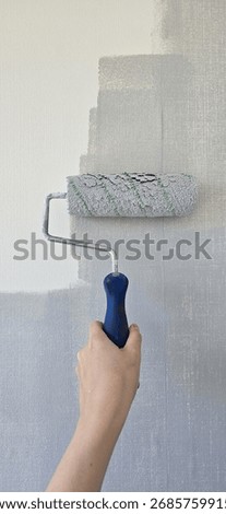 Wall painting with roller using gray paint on white surface. Fresh paint and DIY home renovation concept