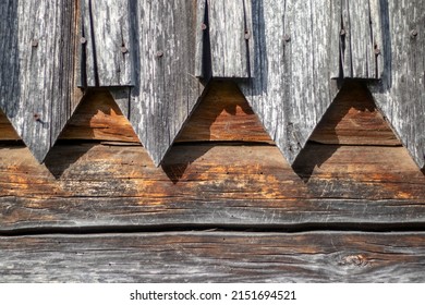 The wall is planked diagonally boards. The edge of the wooden wall is decorated with a carved plinth. Diagonal boards and curly skirting board, side view. Gray colored old boards on the wall 