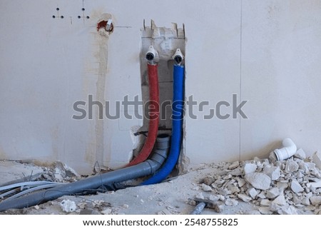 Wall plumbing system installation with exposed red and blue water pipes and drainage components during home renovation. Construction work, building infrastructure and interior remodeling