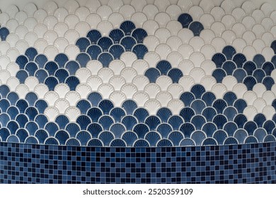 wall with a repeating scallop or fish-scale pattern in blue and white ceramic tiles. The design is geometric and decorative, creating a visually appealing wave-like effect