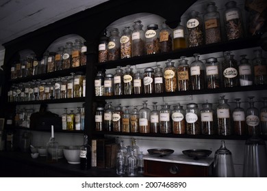 A Wall Of Shelves Filled With Old Glass Apothecary Bottles. The Bottles Are Labeled And Filled With Various Herbs.