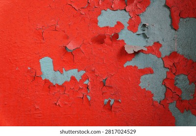 A wall surface with peeling red paint revealing pale blue layer beneath, showing cracked texture and aged material deterioration.