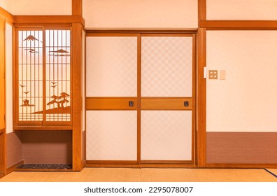 Wall of a typical traditional Japanese room featuring tatami mats covering the floor, fusuma doors and shoji window made of rice paper with wooden decorations evocating a landscape of the mount Fuji.