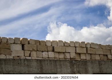 A Wall Under Construction From Bricks And The Blue Sky Behind. An Unfinished Construction In Summer Time.no Money For House.saving, Credit, Rent Or Buy A House. Finish House Building 