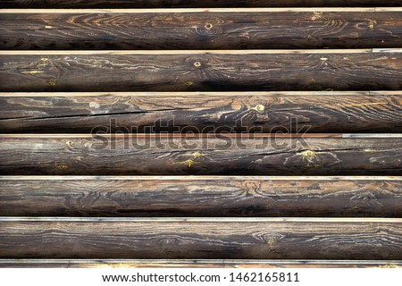 Wall from wooden logs. Background with copy space. Horizontal lines of dark brown weathered wood material. Place for custom text. Log house exterior. Green buulding concept.