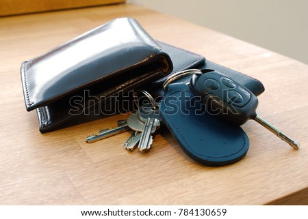 Wallet, car key, house keys and mobile phone on a table together in such a way that looks like someone is about to leave or has just arrived. 