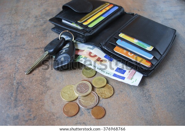 Wallet with cash and credit cards,\
euro coins and car keys on the brown wooden\
background.