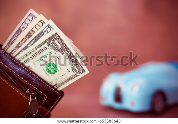 Wallet with dollars banknote and blurred\
toy car on the background - Car expenses\
concept