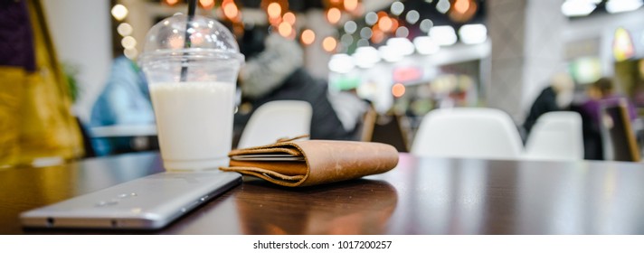 wallet mobile and cup with milk shake on table in cafe