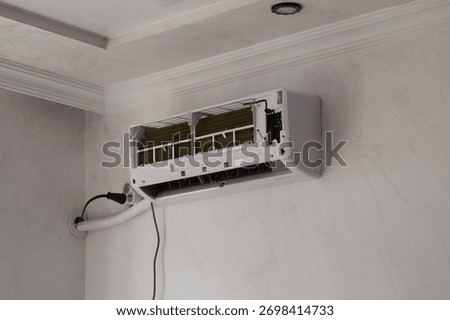 Wall-mounted air conditioner unit opened for repair and filter cleaning. Concept of home maintenance, energy efficiency, cooling system service, and air quality improvement.