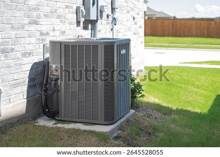 Wall-mounted electrical boxes power control and outdoor HVAC condenser unit with insulated coil foil duct for heating and cooling on concrete pad beside brick wall new house in Princeton, Texas. USA