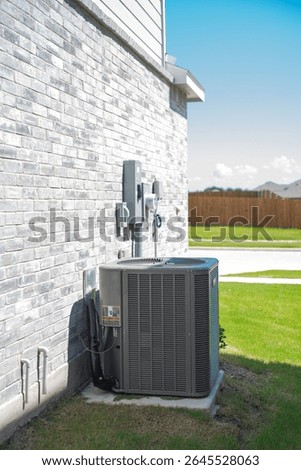 Wall-mounted electrical boxes power control and outdoor HVAC condenser unit with insulated coil foil duct for heating and cooling on concrete pad beside brick wall new house in Princeton, Texas. USA