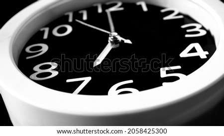 wall-mounted office clock at an angle. time shows 7 am. black and white photograph of a wall clock.
