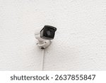 A wall-mounted security camera on a white textured surface, perfect for home surveillance. Its sleek design ensures effective monitoring and safety.