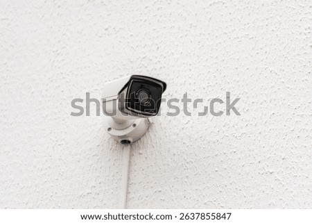 A wall-mounted security camera on a white textured surface, perfect for home surveillance. Its sleek design ensures effective monitoring and safety.