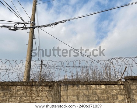 Walls, barbed wire, electric poles, electric lines, blue sky,