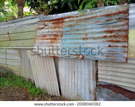 the walls are made of a thin layer of zinc that has been partially rusted in red and gray in the yard of the house