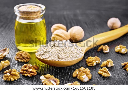 Walnut flour in a spoon, nuts on the table and oil in a glass jar on background of wooden board