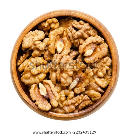 Walnut kernel halves, in a wooden bowl. Shelled, dried seeds of the common walnut tree Juglans regia, used as snack or for baking. Close-up, from above, isolated on white background, macro food photo.