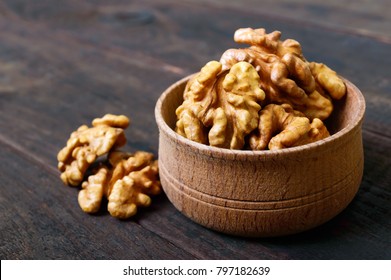 Walnut kernels in a wooden bowl on a dark wooden background. Close-up.