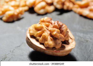 Walnut whole, half shelled close up with shelled walnuts on black slate background. Selective focus.