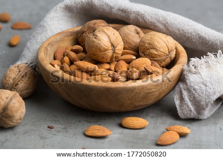 
walnuts and almonds in a wooden plate on a gray background
