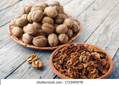   Walnuts in a ceramic plate and walnut kernels in a clay plate on a wooden table. Two ceramic plates in walnuts on a wooden table. Wood background.                             