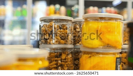 Walnuts and dried mango slices are displayed in clear jars on a supermarket shelf, offering a healthy and convenient snack option for customers