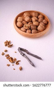 Walnuts heap food in wooden bowl with half peeled nut, cracked nutshell, near to vintage nutcracker on white background, angle view, healthy food concept