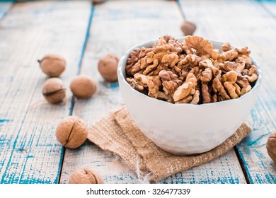 Walnuts in shells and cracked nuts in a bowl on a painted white and blue table