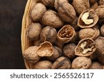 Walnuts in a wicker basket on a dark wooden background. Nuts in an oval basket, top view. Heap of walnuts in shells, close-up, background. Healthy eating. Harvest, agriculture