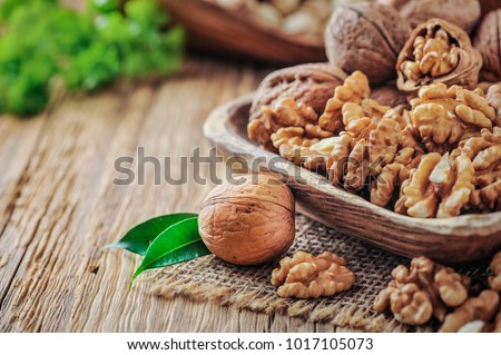 Walnuts in wooden bowl. Whole walnut on wood table with green leaves