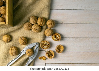 Walnuts in a wooden box, which stands on an old rustic sack, also scattered on a white table nearby is a cracker of walnut.