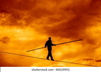 Wandering tightrope walker playing on yellow sky background. Silhouette of Equilibrist businessman with pole on the rope