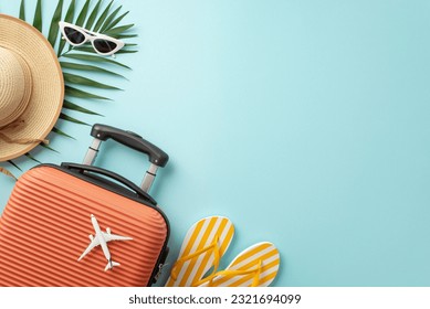 Wanderlust getaway. Orange suitcase seen from top view, miniature airplane, beach accessories, eyewear, hat, flip-flops, palm leaves on a pastel blue background, offering space for text or advertising - Powered by Shutterstock