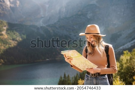 Wanderlust and travel concept. Stylish traveler girl in hat looking at map, exploring woods. Young oman with backpack travelling at lake in forest. 
