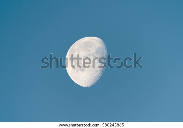 Waning moon in blue sky in early morning, showing\
detailed craters