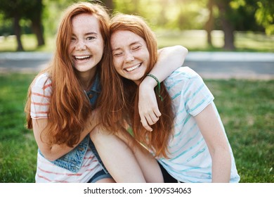 Wanna hug her forever. Portrait of happy and carefree two twin sisters with natural red hair and freckles, laughing out loud and cuddling, fooling around while resting in park on fresh green grass. - Powered by Shutterstock