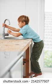 I Want To Get Some Water.... A Cute Young Boy Climbing The Kitchen Counter To Get To The Tap.