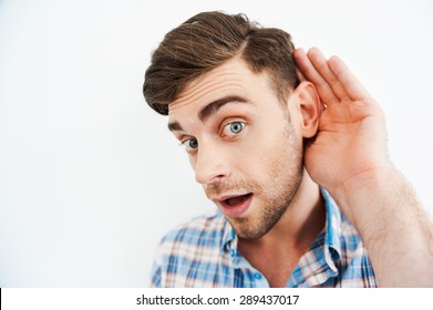 I Want To Know Everything! Curious Young Man Holding Hand Behind Ear And Looking At Camera While Standing Against White Background