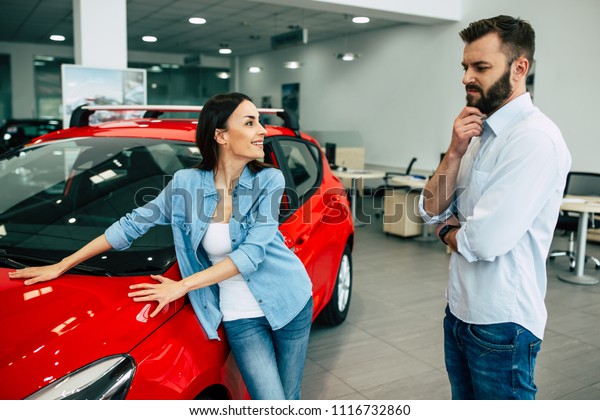 I want this\
one car, please! Young couple in dealership. Husband thinking about\
choice the car of his wife.