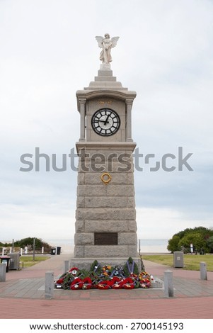 War memorial clock tower adorned with wreaths commemorating ANZAC Day and remembrance, standing under an overcast sky