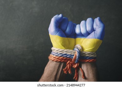 War in Ukraine. Male hands in the colors of the flag of Ukraine tied with a rope in the colors of the flag of Russia on a dark background. Conceptual image of violence, occupation, aggression